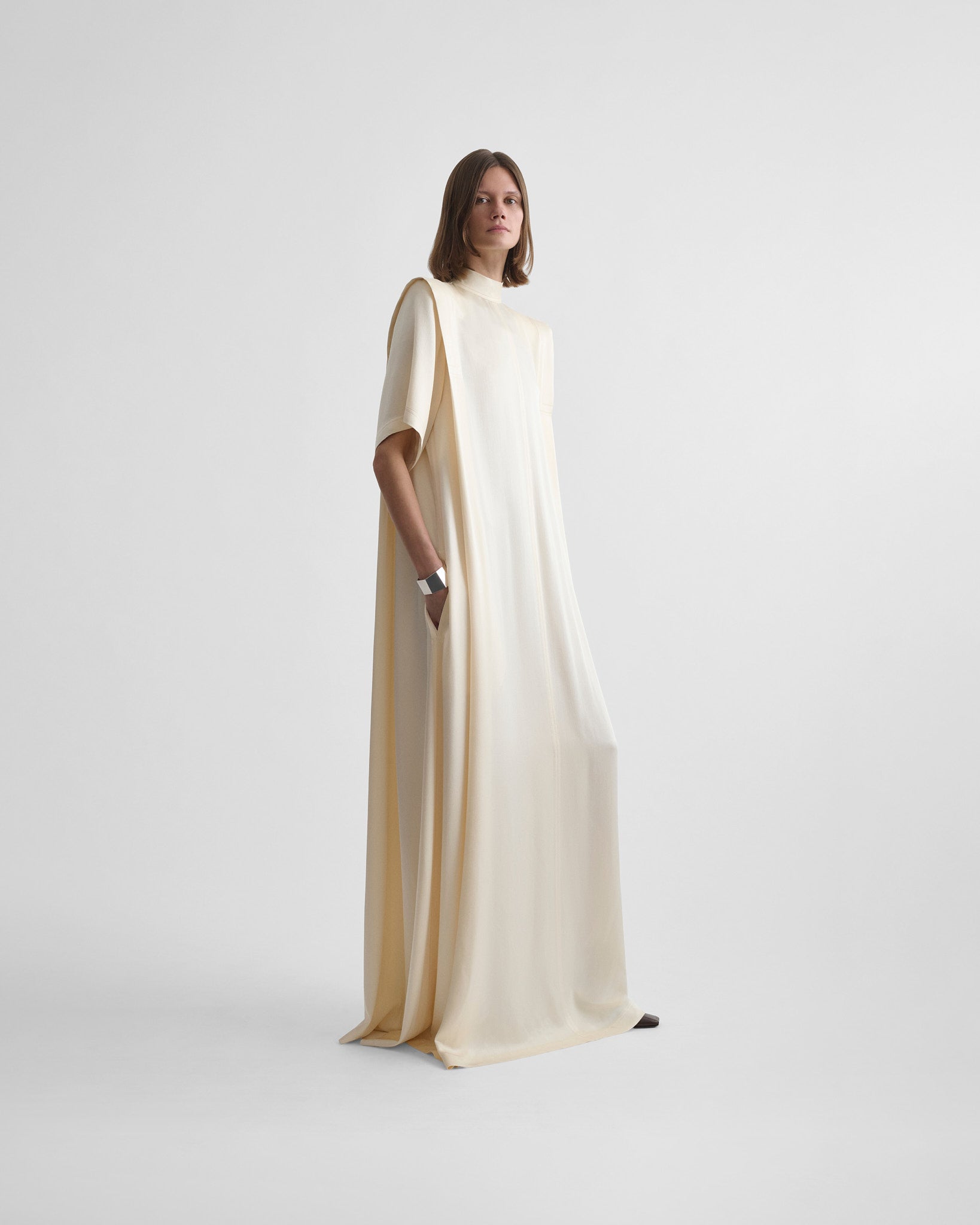 Angled front view of model wearing folded shoulder dress in vanilla satin back crepe
