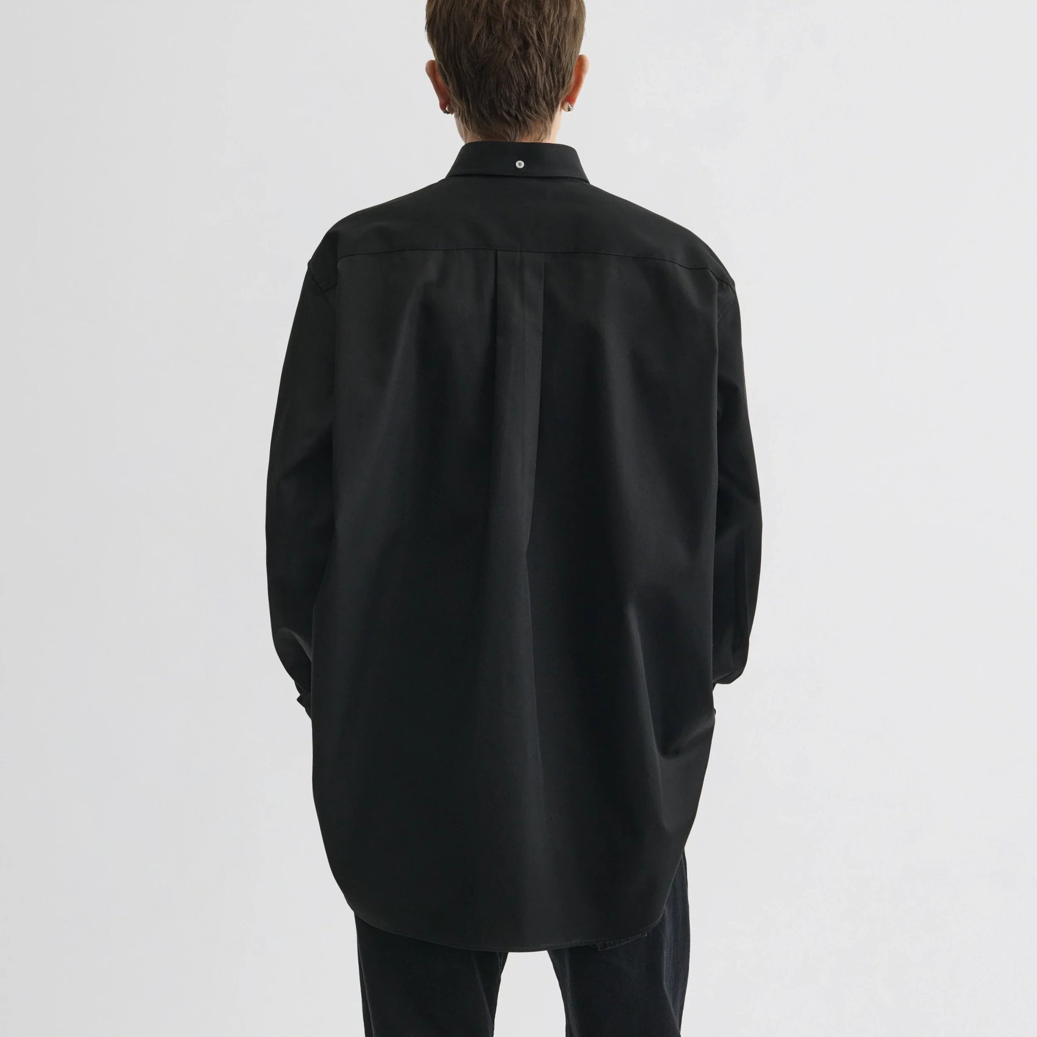 Back view of model wearing button collar shirt in black cotton.
