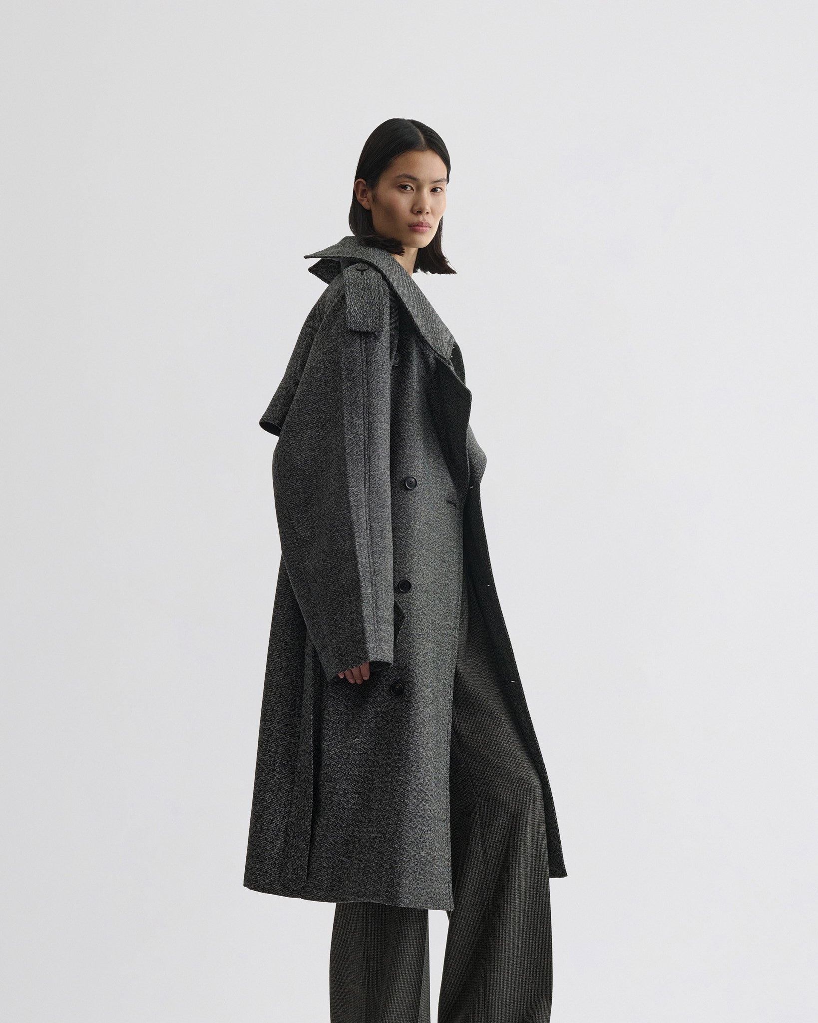 Side view of model wearing padded trench coat in salt and pepper wool.