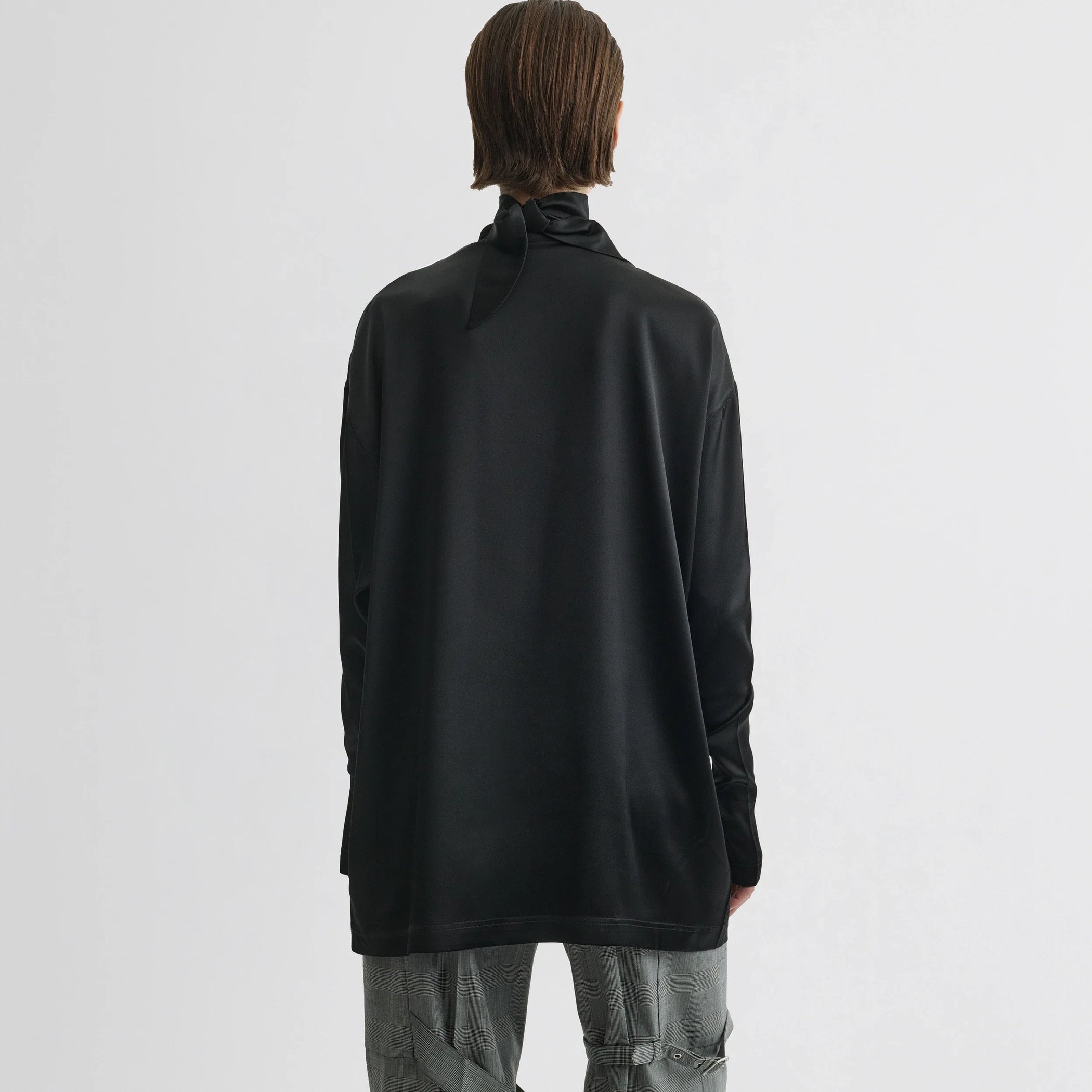Back view of model wearing liquid knot collar top in black silk.