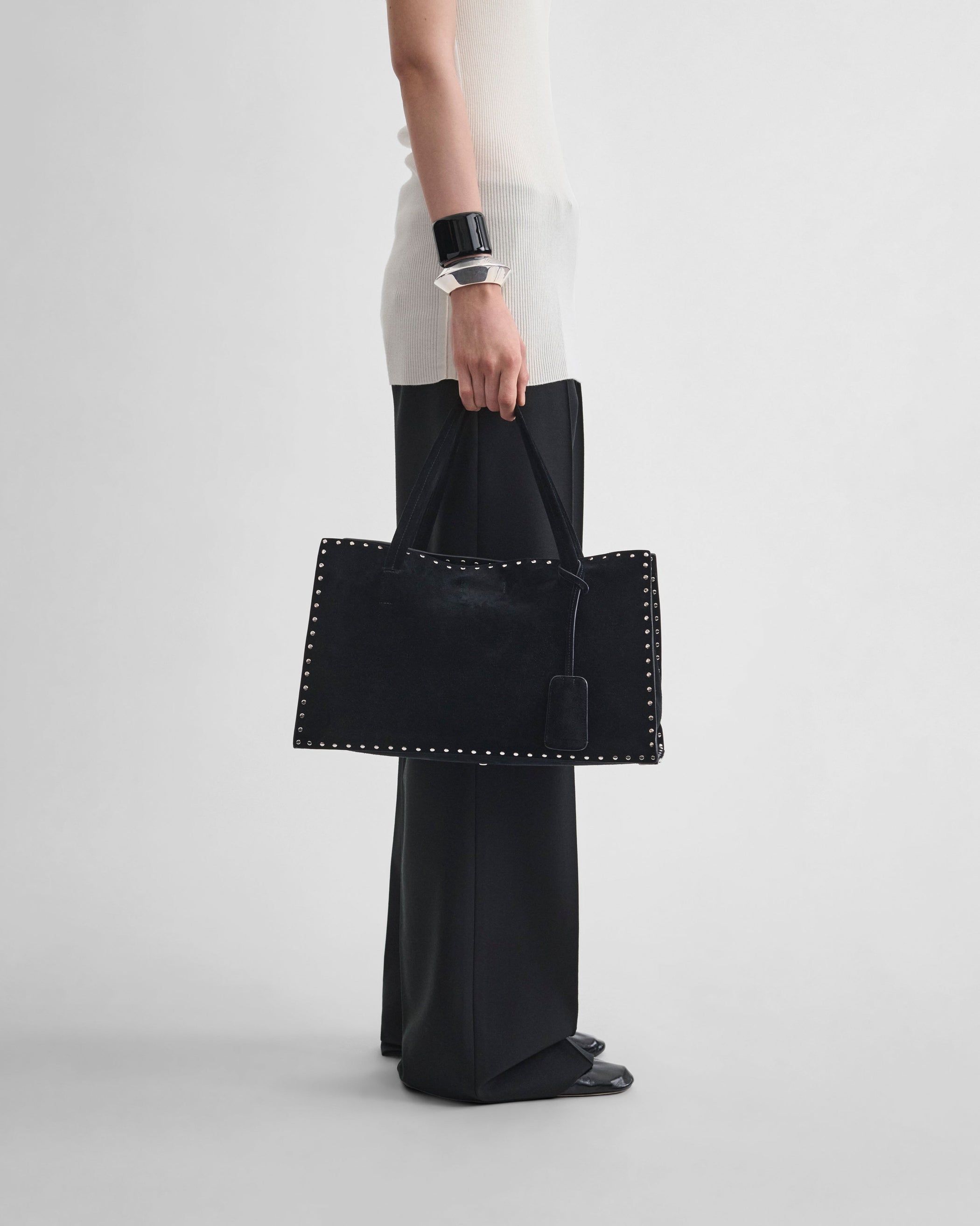 Side view of model holding SMALL STUD CABAS in black suede